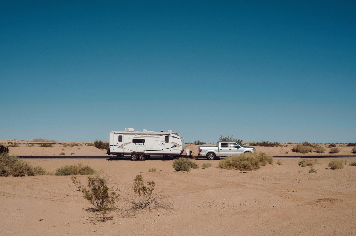 Pickup and travel trailer stopped on open desert ground with scrub and distant hills